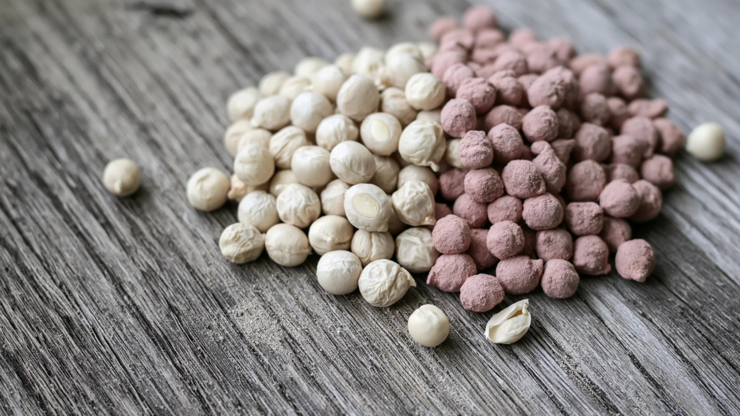 Deux tas de pois secs côte à côte sur une planche de bois gris : à gauche des graines nues de couleur naturelle, à droite les mêmes graines enrobées d'un rose crayeux de traitement
